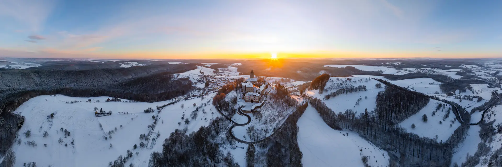 Luftbild der Leuchtenburg über Kahla im Schnee, tief stehende Sonne über der verschneiten Hügellandschaft