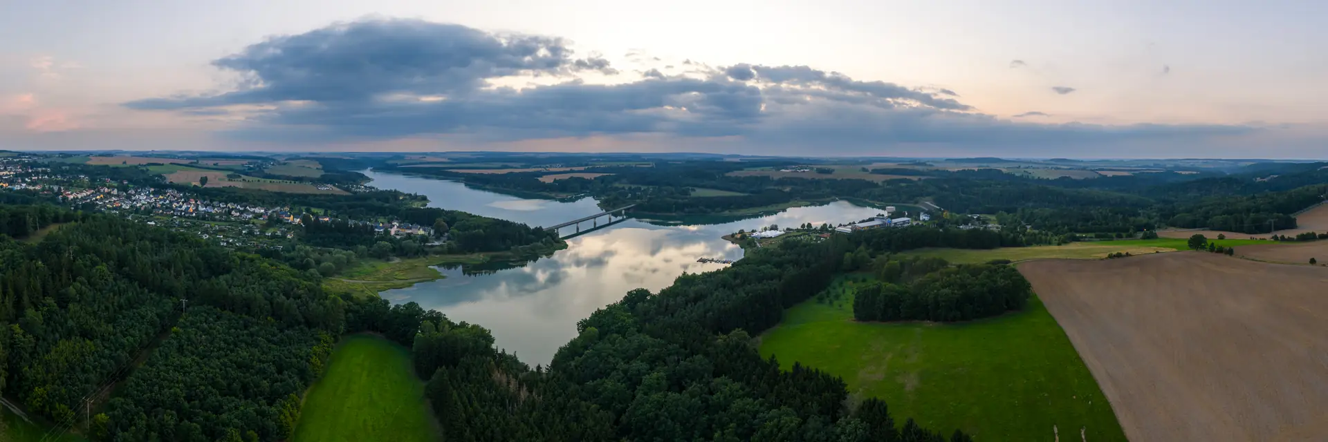 Luftbild des Zeulenrodaer Meeres in der Abenddämmerung, Wälder und Felder rahmen den Stausee mit Brücke
