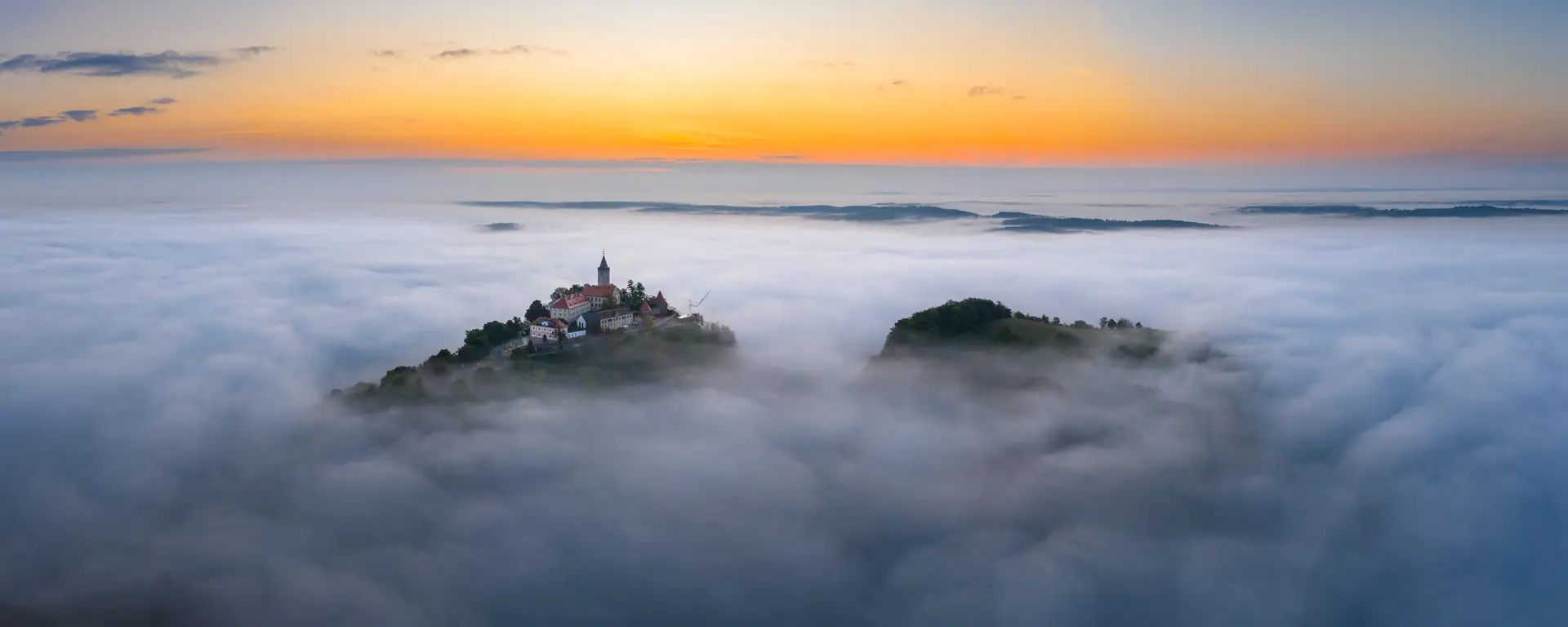 Leuchtenburg über dem Nebelmeer bei Sonnenaufgang, oranger Himmel über dem Horizont