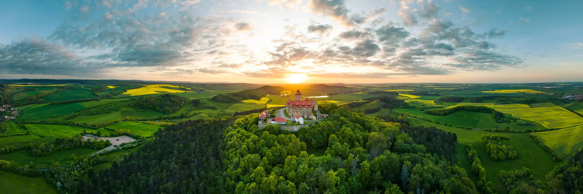 Die Wachsenburg auf ihrem bewaldeten Kegel, umgeben von Feldern im Abendlicht