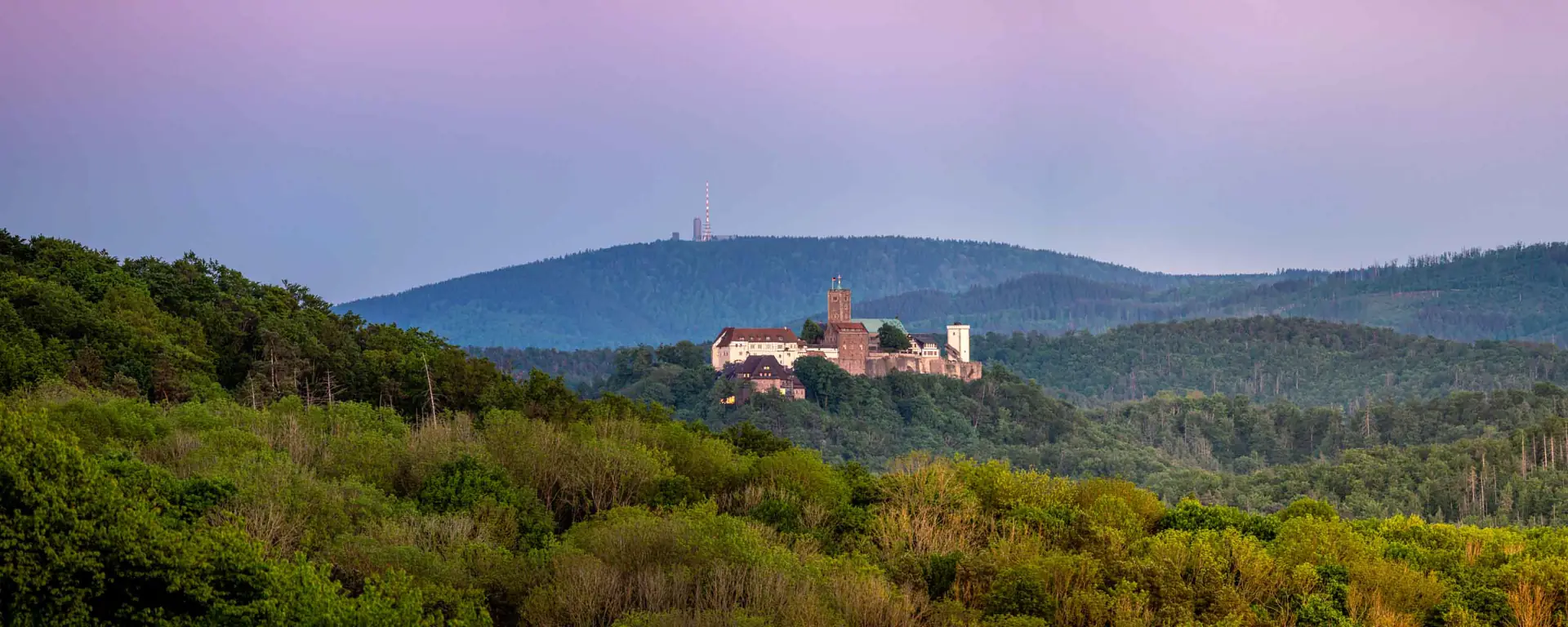 Wartburg bei Eisenach vor violettem Dämmerhimmel, im Hintergrund der Inselsberg